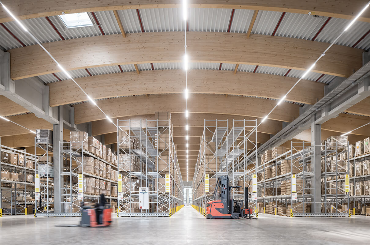 Symmetrischer Blick in die gut ausgeleuchtete Lagerhalle. Die Decke ist wunderschön gebogen, mit einer architektonisch sehr schönen Holzkonstruktion.