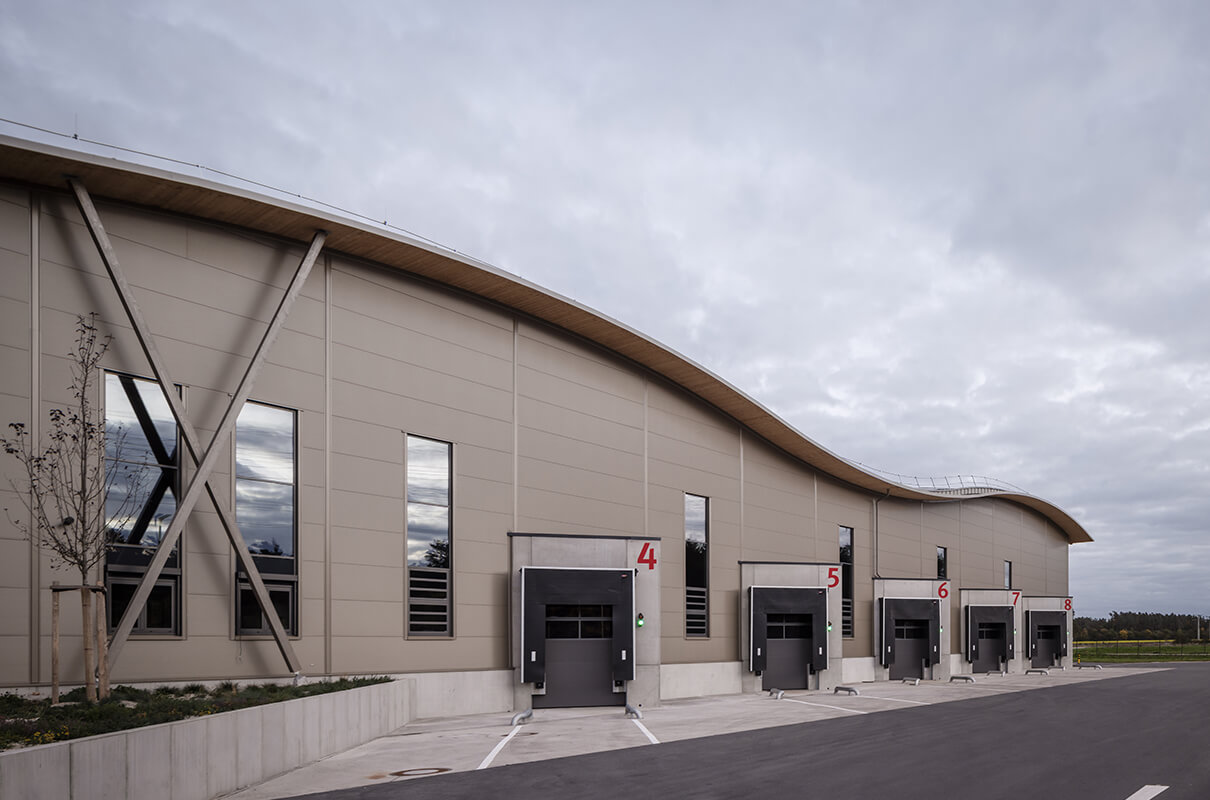 Ansicht der Lagerhalle der Hammerbacher GmbH, mit wellenförmigem Dach. Zu sehen sind explizit 5 Liefertore mit den einzelnen roten Nummern.
