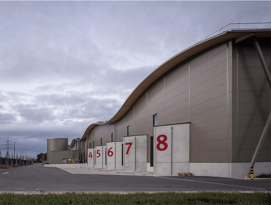 Ansicht der Lagerhalle der Hammerbacher GmbH seitlich von hinten nach vorne mit den einzelnen Anlieferungsplätzen. Jedes Tor hat eine große rote Ziffer.
